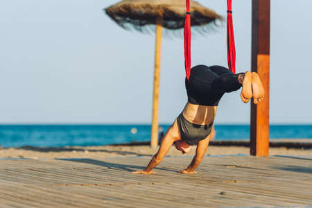 young woman doing yoga exercise on the ground outdoors by the sea at sunsetの写真素材