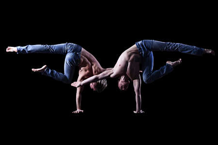 two twin brothers in blue jeans with a naked torso perform acrobatic elements, black backgroundの写真素材
