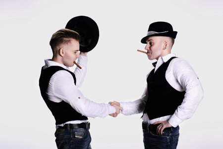 two twin brothers in gangster style posing. hats, vests, white shirts. white background.の写真素材
