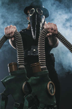 a girl in a plague mask and a black hat holds gas masks in her hands. against the background of smokeの写真素材
