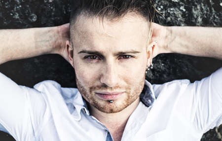 handsome guy in a white shirt holds his hands behind his head and posing. close-up