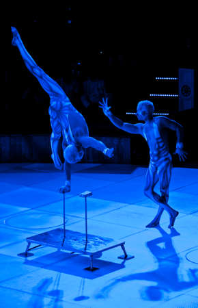 twins acrobats in neon costumes stand on their arms, ultraviolet makeup