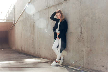 beautiful blonde in a black cape posing against the background of a concrete wallの写真素材
