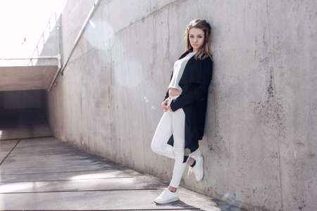 beautiful blonde in a black cape posing against the background of a concrete wallの写真素材