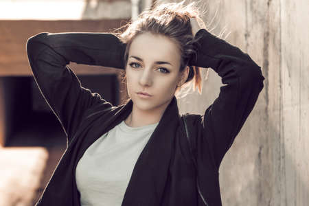 beautiful blonde in a black cape posing against the background of a concrete wallの写真素材