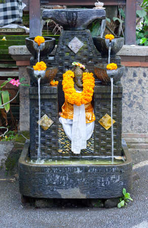 indonesian exotic foliage background with traditional elephant fountain sculpture, patterns, fabric, flowers and giftsの写真素材