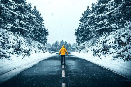 Person with a yellow coat in the middle of a road in the middle of a snow storm in a winter...