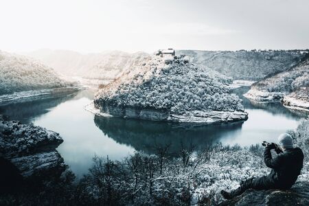 Photographer taking pictures in a snowy landscape of a river meanderの写真素材