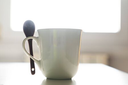White coffee mug with a spoon with the window light in the backgroundの写真素材