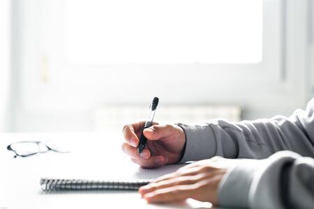 Student writing in a notebook doing homework at his desk at homeの写真素材