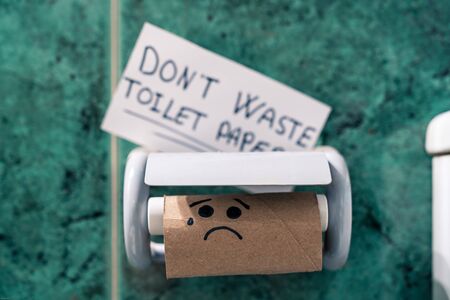 Toilet paper roll finished in the bathroom with a picture of a sad face due to coronavirus panic. Don't waste toilet paper it's written on paper.の写真素材