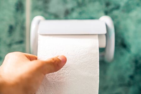 Hand holding toilet paper in a roll holder.の写真素材