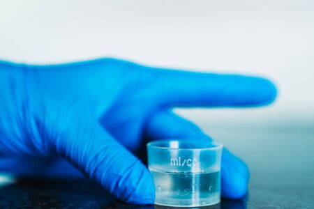 Measuring cup full of disinfectant held with hand with blue latex glove.の写真素材