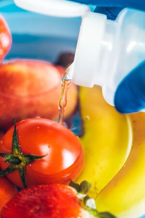 Hand pouring bleach into a plastic bowl with different fruits and water with blue latex gloves in the kitchen . Disinfecting fruits and vegetables to prevent the spread of the coronavirusの写真素材