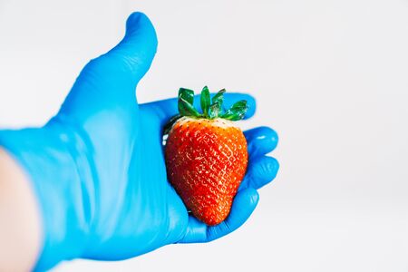 Hand holding a strawberry with blue latex gloves. Disinfecting the fruit to prevent the spread of the coronavirus.の写真素材