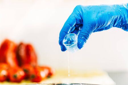 Hand with blue latex gloves pouring disinfectant liquid to decontaminate fruit and vegetables from viruses. Washing the fruit with bleach.の写真素材