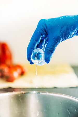 Hand with blue latex gloves pouring disinfectant liquid to decontaminate fruit and vegetables from viruses.の写真素材