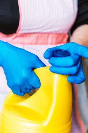 Woman with blue latex gloves and apron opening a yellow bottle of bleach.の写真素材