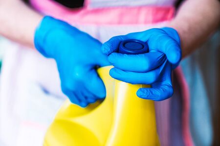 Housewife with blue latex gloves and apron opening a yellow bottle of bleach.の写真素材