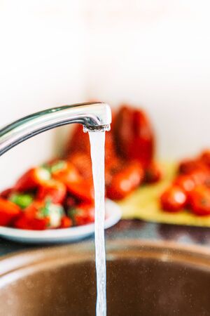 Washing the fruit in the kitchen sink with water. Open tap with tomatoes, strawberries, peppers.の写真素材