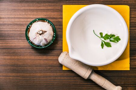 Preparing a recipe to make aioli in a traditional and homemade way. Ingredients and utensils to prepare garlic oil. Garlic head, parsley leaf and a mortar on top of a vintage-style wooden worktop.の写真素材