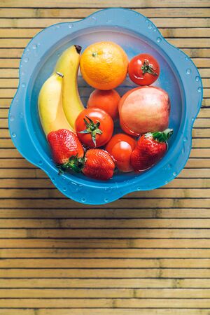 Blue bowl with different fresh and clean fruits on a wooden base. Bananas, tomatoes, apples, strawberries and oranges.の写真素材
