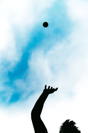 Happy person doing sport by throwing a ball in the air. Silhouette of a carefree boy playing happily with a tennis ball on a beautiful sunny summer day.の写真素材