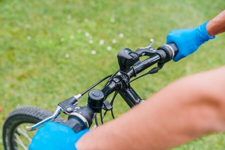 Person cycling outdoors in nature wearing blue latex gloves as a coronavirus prevention measure. Person holding the handlebars of the bicycle.の写真素材