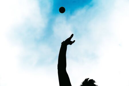 Happy person doing sport by throwing a ball in the air. Silhouette of a carefree boy playing happily...