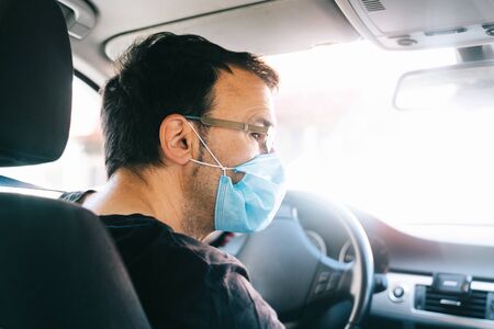 Man wearing protective mask driving. Man in protective mask driving a car in the city.の写真素材