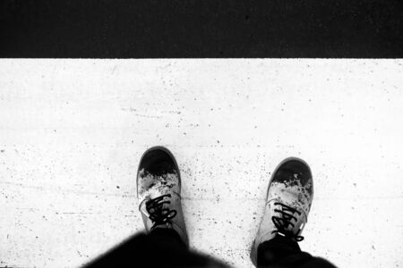 Zenith view of a person waiting to cross a zebra crossing. Feet of a person in wet brown leather boots. Conceptual image in black and white.の写真素材