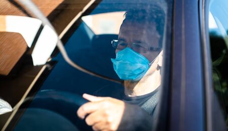 Man wearing protective mask driving. Man in protective mask driving a car in the city.の写真素材