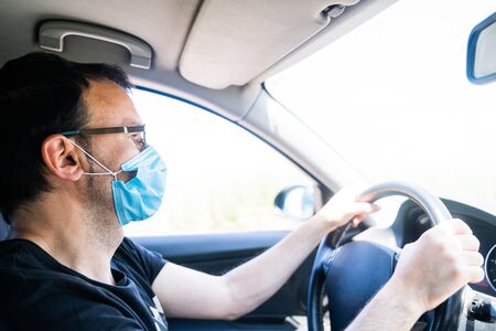 Man wearing a protective mask driving. Driver wearing a mask inside the car holding the steering...