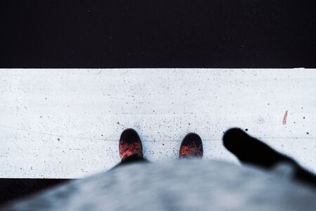 Zenith view of a person's feet in wet brown leather boots and an umbrella on top of the white strip of a zebra crossing on a road.の写真素材