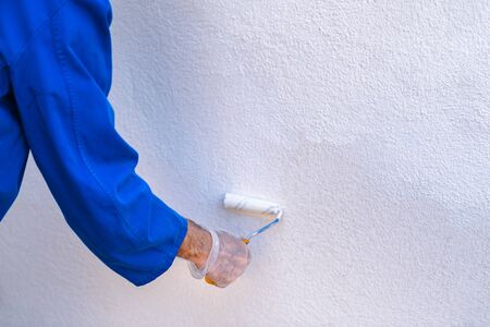 Man painting the wall of the house. Hand holding a roller with white paint. Concept of painting and...