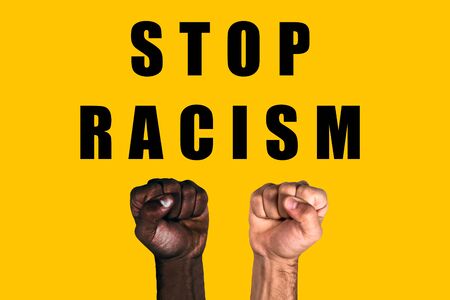 African black fist and caucasian white fist raised calling for freedom and equality on a yellow background. Multicultural fists raised. Stop racism.の写真素材