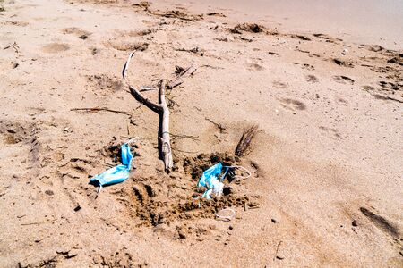 Medical face masks used and thrown on the sand of an empty beach. Covid coronavirus contamination.の写真素材