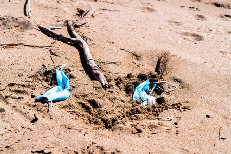 Medical face masks used and thrown on the sand of an empty beach. Covid coronavirus contamination.の写真素材
