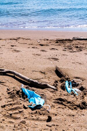 Medical face masks used and thrown on the floor of an empty beach. Covid coronavirus contamination in the sea.の写真素材