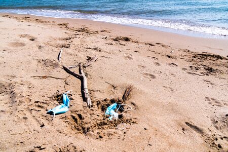 Medical face masks used and thrown on the sand of an empty beach. Covid coronavirus contamination in thea sea.の写真素材
