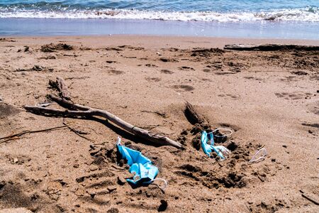Medical face masks used and thrown on the floor of an empty beach. Covid coronavirus contamination in the sea.の写真素材