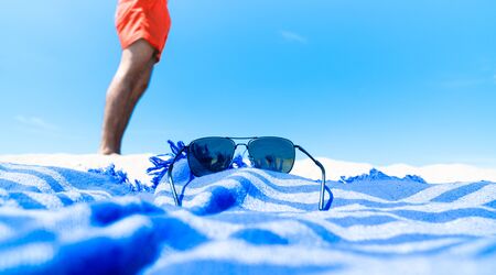 Person enjoying the summer beach holiday wearing a red swimsuit, blue beach towel and sunglasses on the sandy beach on a sunny day.の写真素材