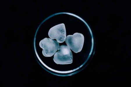 Elegant glass cup with heart shaped ice cubes on black background. Top view with copy space. Luxurious service of alcoholic drinks and smoothies.の写真素材