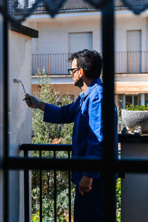 Mature man painting the terrace of the house observed through the window from inside the house. Vertical photo of concept of painting and reforming the corners of the house.の写真素材