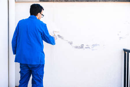 Back view of mature man painting white wall. Concept of painting and reforming the corners of the house.の写真素材