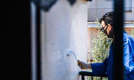 Mature man painting the terrace seen through the window of the house.の写真素材