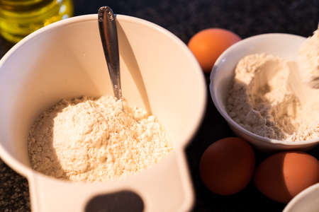 White bowls filled with flour and eggs and oil on top of the kitchen marble. Preparation for making a homemade cake in home.の写真素材