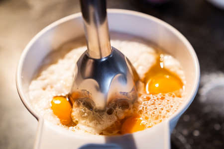 Whipping the eggs and flour in a bowl with a hand blender to prepare a recipe. Prepare a homemade cake at home.の写真素材