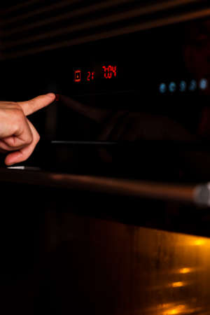 Female hand turning on the oven to make a cake at home.の写真素材