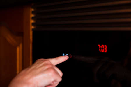Female hand turning on the oven to make a cake in the kitchen. Close up side view photo.